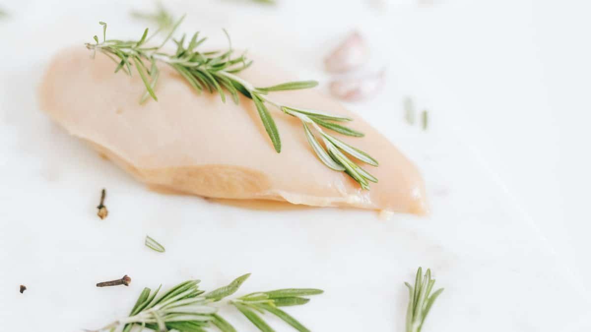 Healthy raw chicken breast garnished with rosemary on a marble surface.