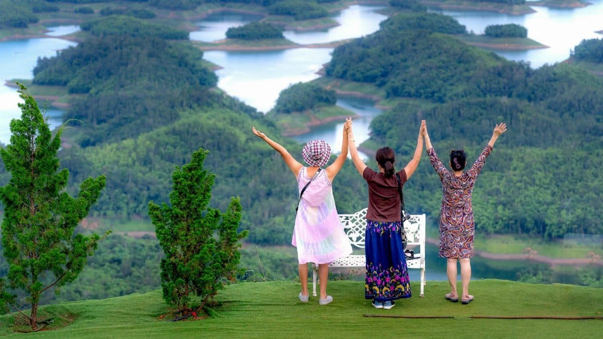 Three women raise their arms in celebration while overlooking lush islands and lakes, symbolizing adventure and togetherness.