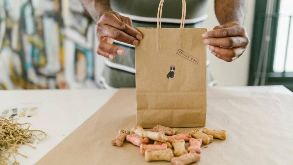 Hands pack colorful dog treats in a thank you kraft paper bag.