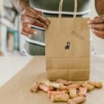 Hands pack colorful dog treats in a thank you kraft paper bag.