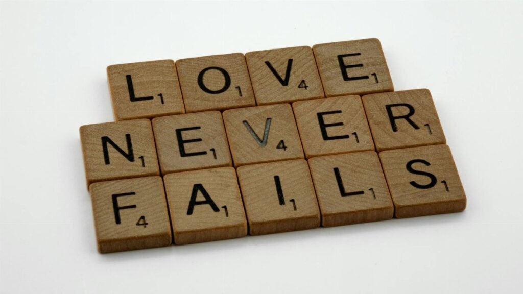 Wooden Scrabble tiles spelling out 'Love Never Fails' on a white background.