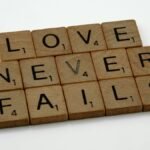 Wooden Scrabble tiles spelling out 'Love Never Fails' on a white background.