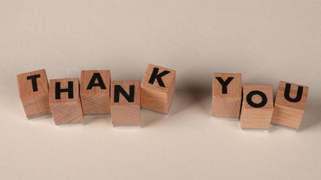 Wooden blocks spell 'THANK YOU' on a soft beige background, expressing gratitude.