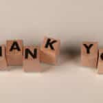 Wooden blocks spell 'THANK YOU' on a soft beige background, expressing gratitude.