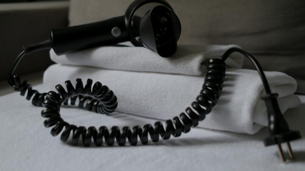 A coiled hair dryer placed on folded white towels, suggesting a hotel setting.