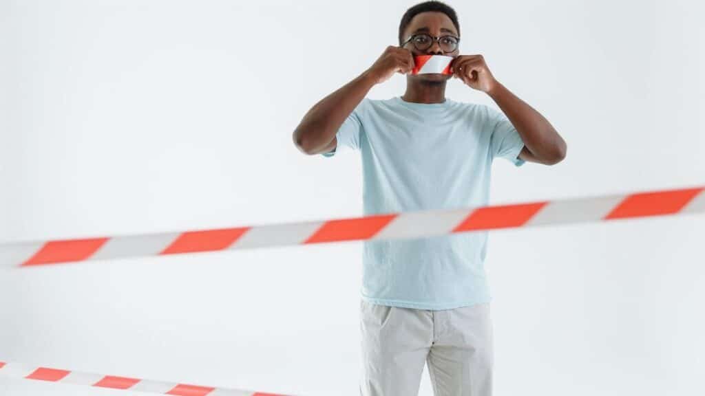 Adult man posing with barricade tape on mouth, studio shot. Conceptual image of silence and protest.