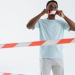 Adult man posing with barricade tape on mouth, studio shot. Conceptual image of silence and protest.