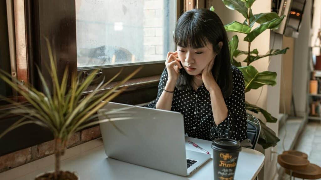 Asian woman focused on work in a modern office setting with laptop and coffee.