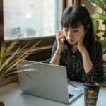Asian woman focused on work in a modern office setting with laptop and coffee.