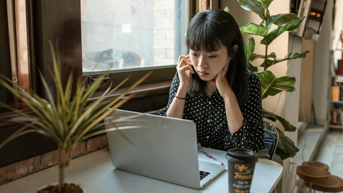 Asian woman focused on work in a modern office setting with laptop and coffee.