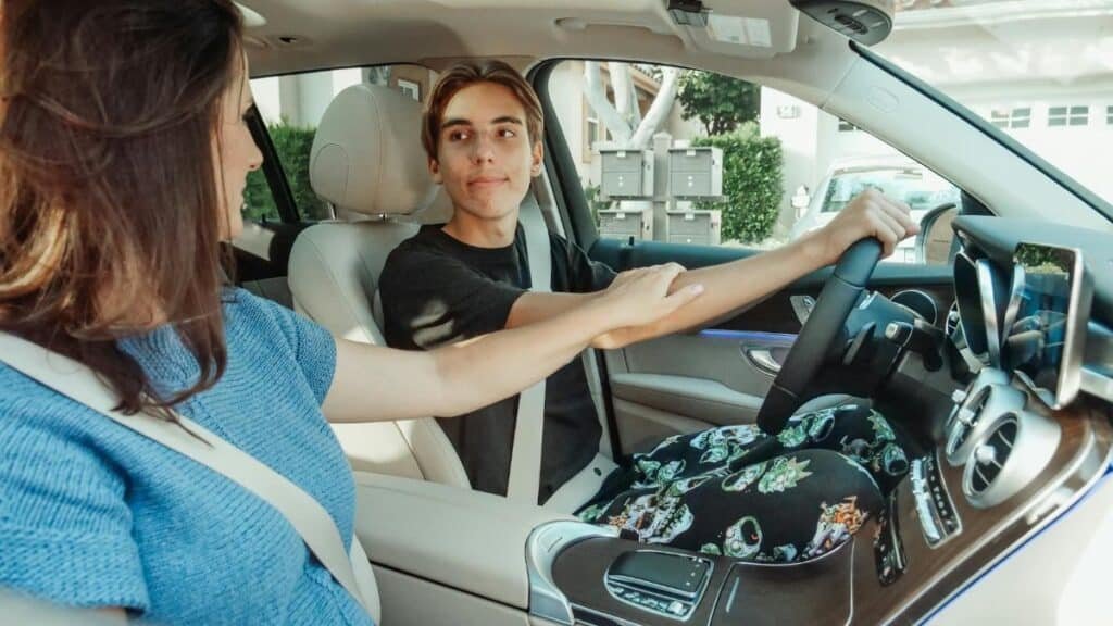 A mother supports her teenage son as he learns to drive in a car