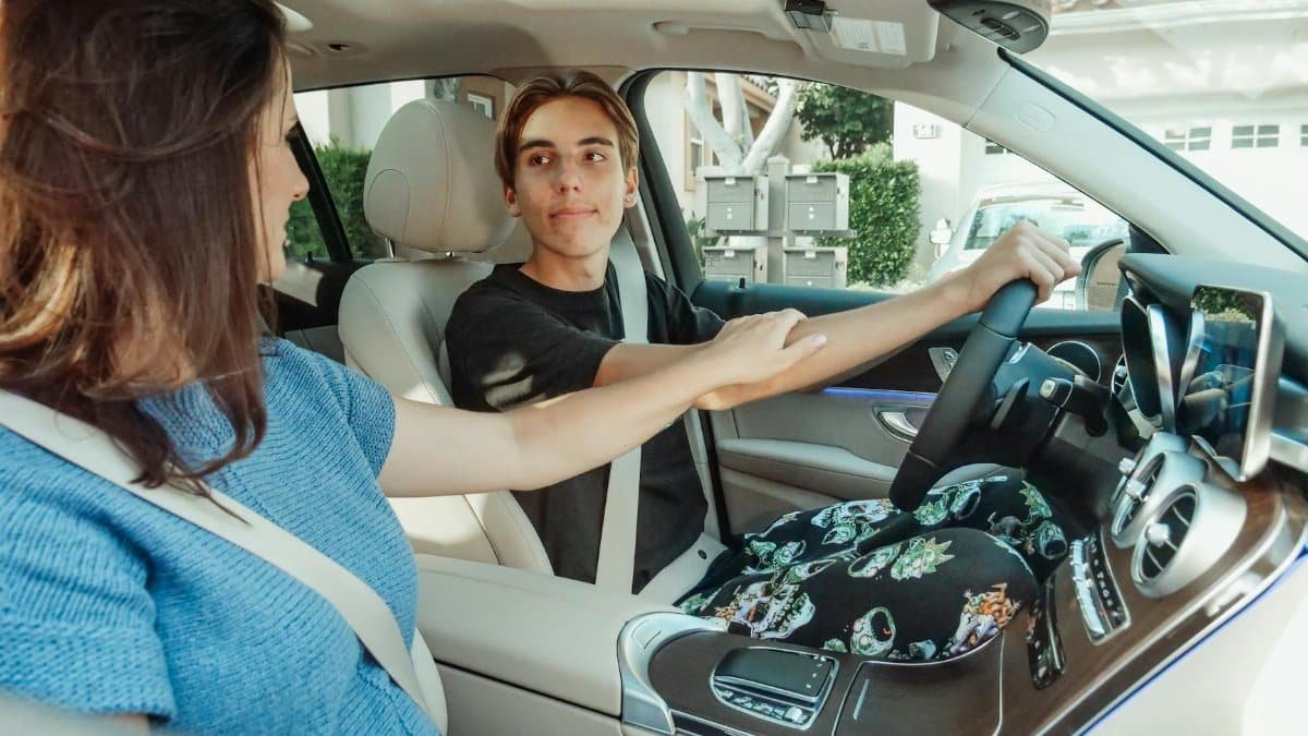 A mother supports her teenage son as he learns to drive in a car