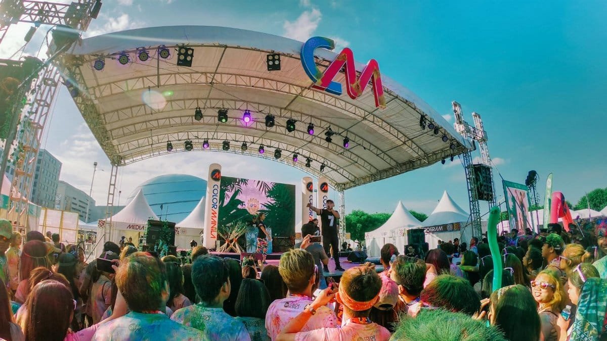 Colorful outdoor music festival with a lively crowd enjoying live performances under a sunny sky.