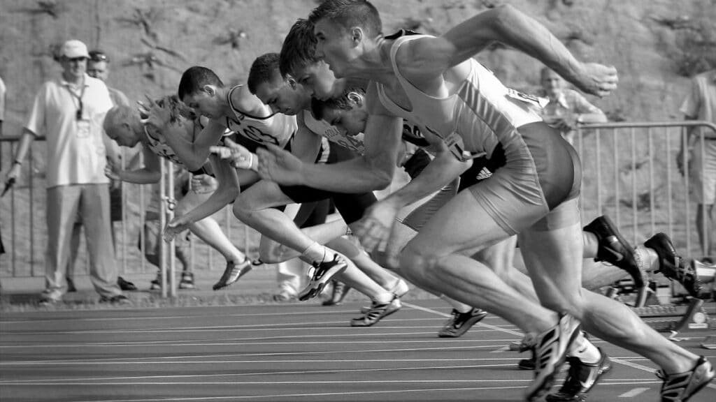 Athletes burst from the blocks during a sprint race, captured in monochrome.