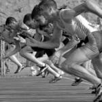 Athletes burst from the blocks during a sprint race, captured in monochrome.