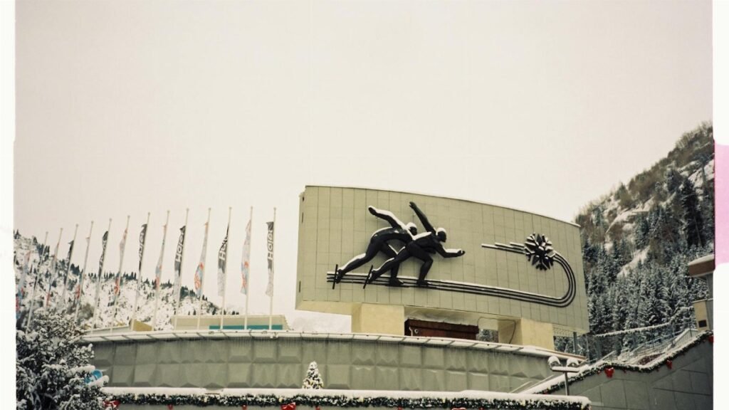 Sculpture of ice skaters at snowy winter sports venue, flags in background.