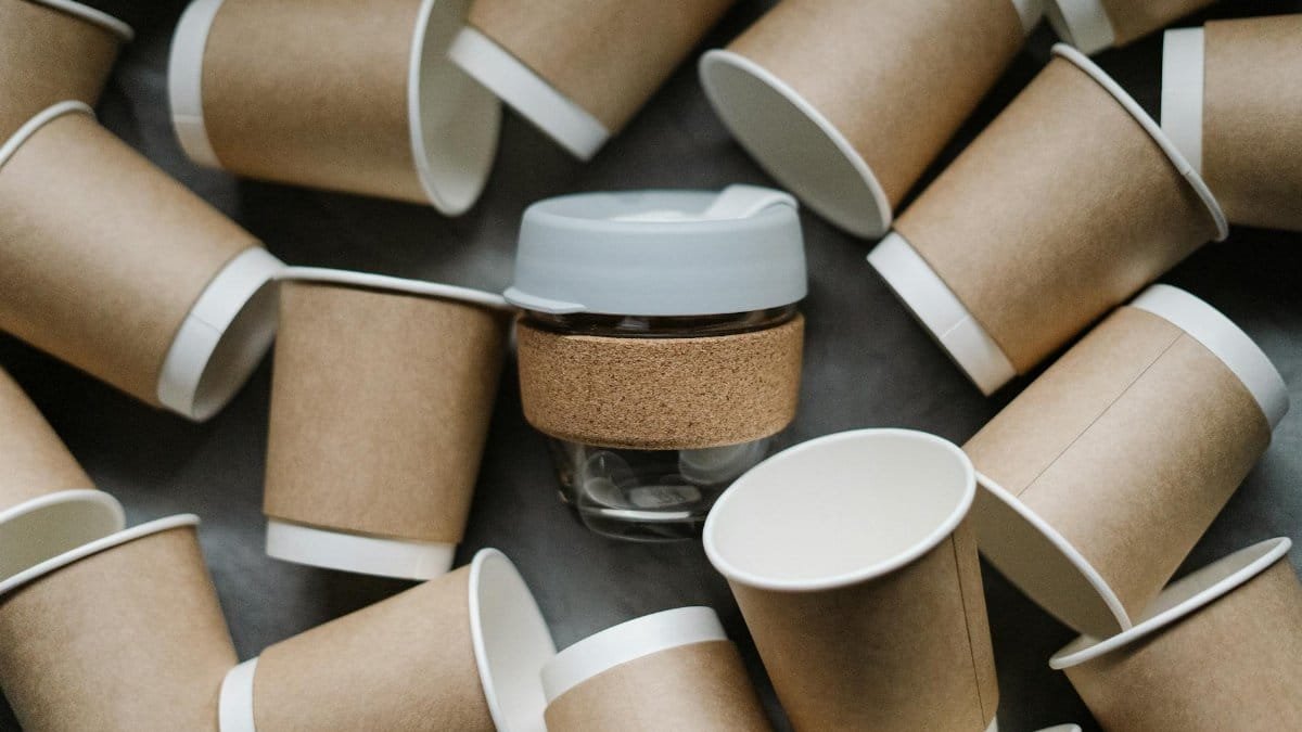 A reusable cup surrounded by disposable paper cups emphasizes zero waste and sustainability.