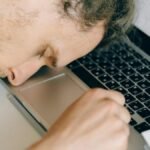 Exhausted employee resting head on laptop keyboard due to burnout and stress.