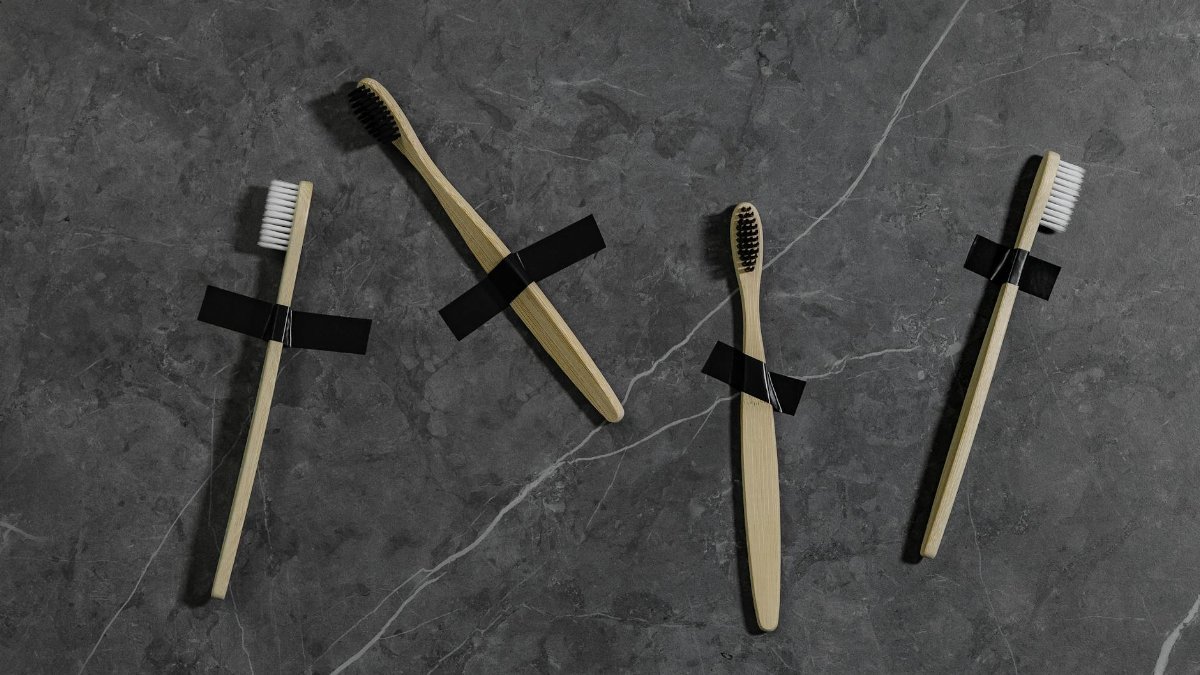 Top view of eco-friendly bamboo toothbrushes taped on a marble surface, promoting sustainable dental care.