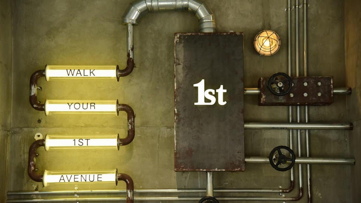 An artistic industrial wall design featuring metal pipes and illuminated words.