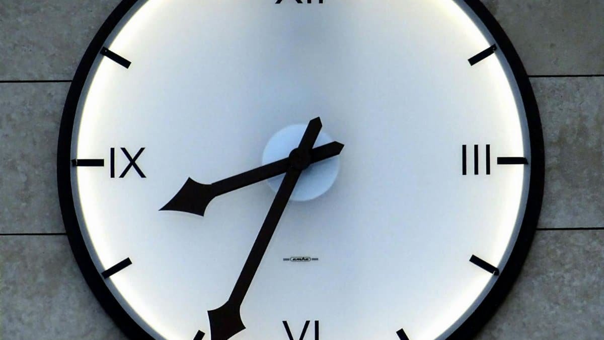 Close-up of a modern wall clock with Roman numerals and backlit design, emphasizing timekeeping precision.