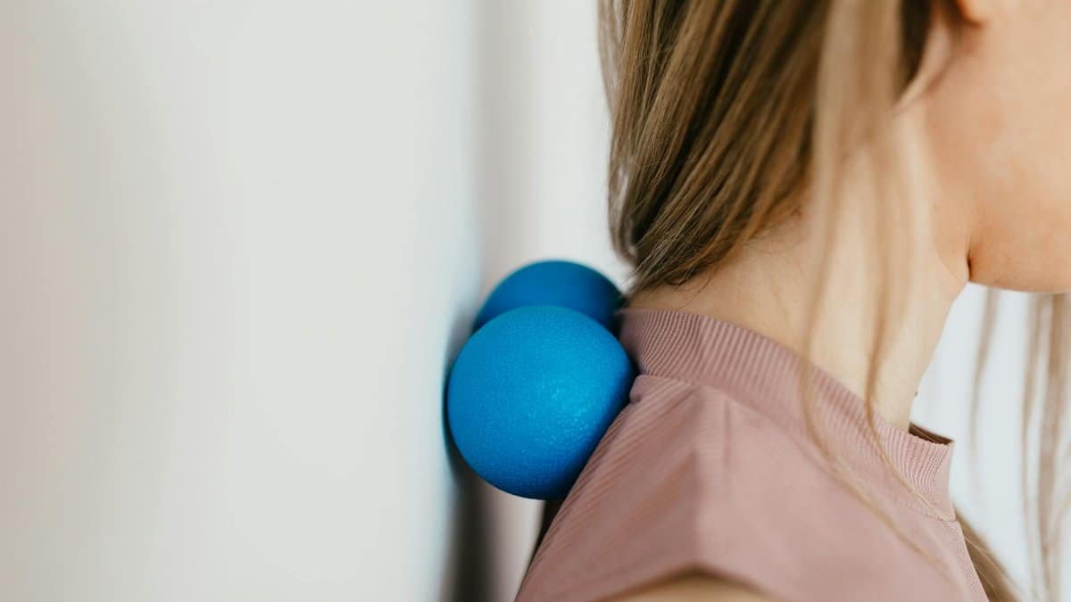 Close-up of woman using blue massage balls for neck relief against a wall.