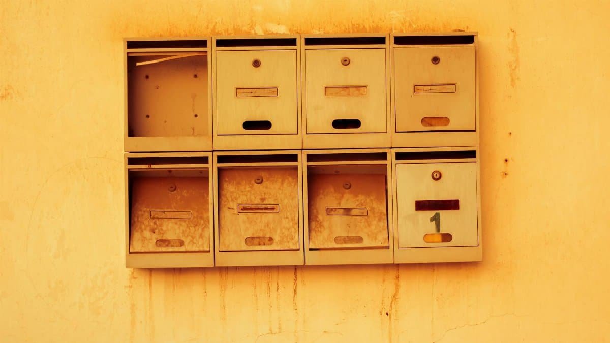 Old metal mailboxes attached to a textured wall with a warm vintage tone.