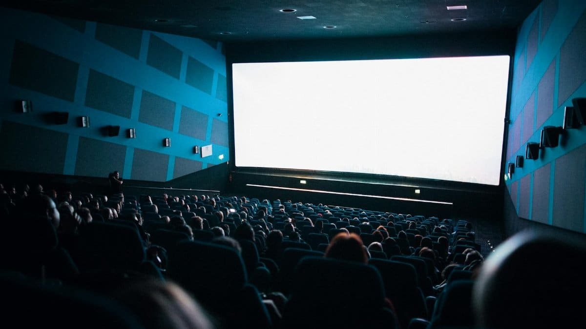A crowded cinema audience seated in a theater watching a movie on a large screen.