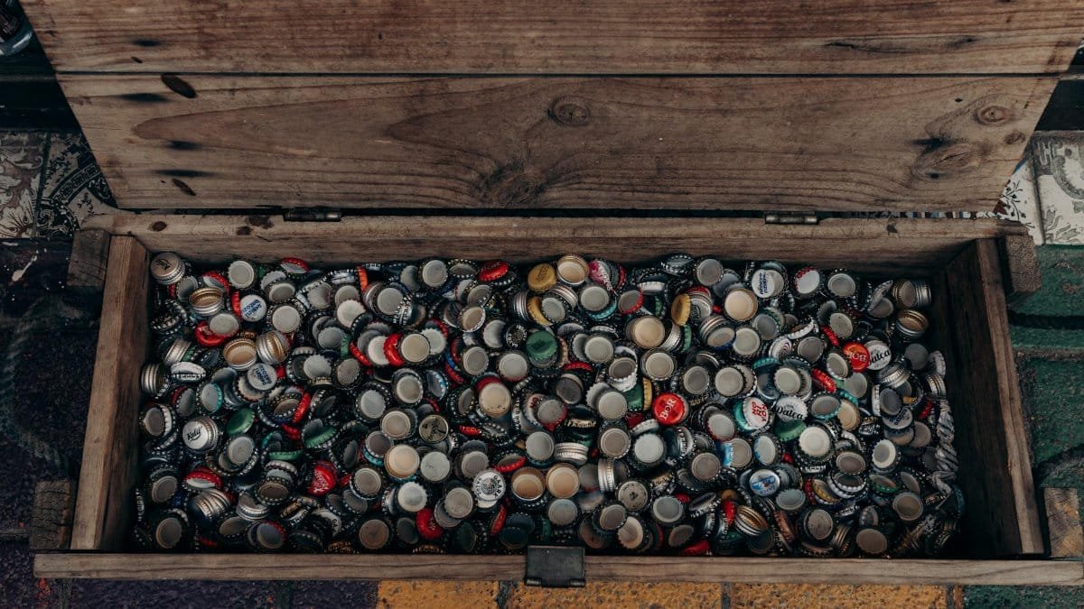 A top view of a wooden chest filled with assorted vintage beer bottle caps.