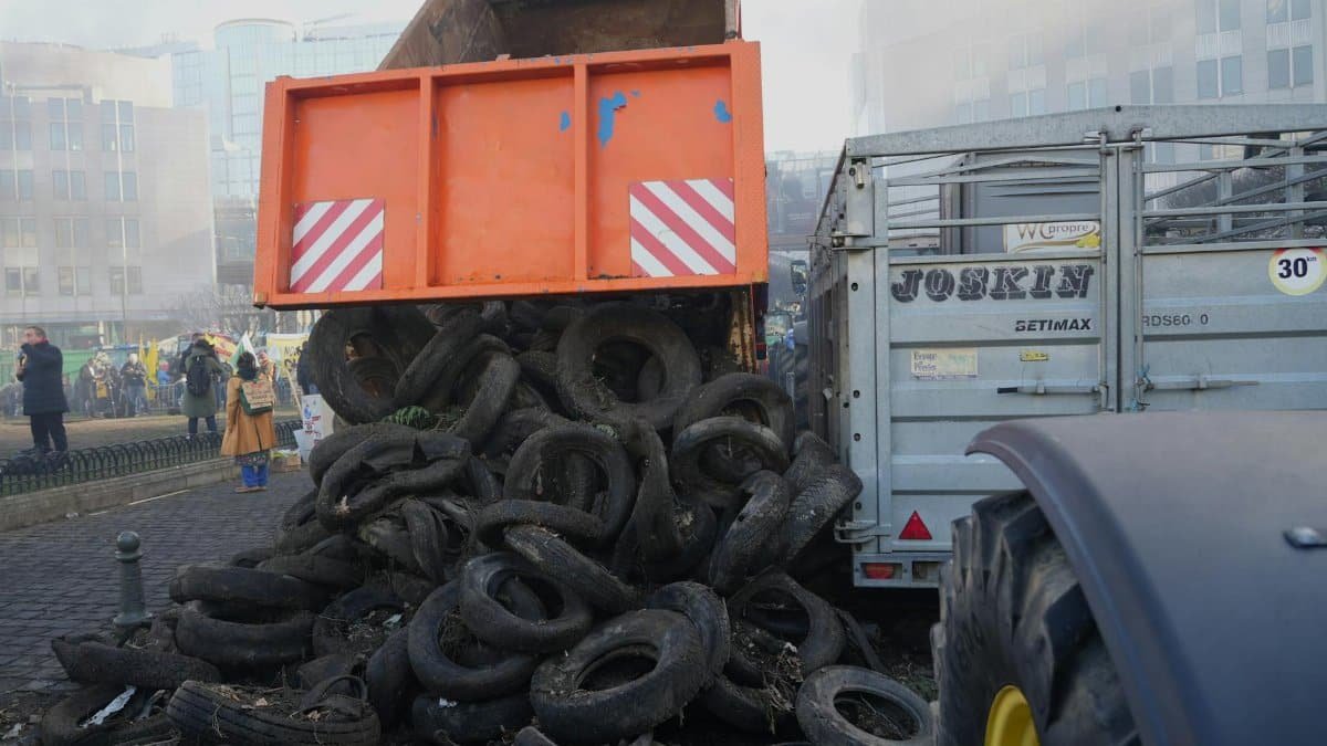 Protest in city street featuring dump truck unloading tires, surrounded by people and buildings.