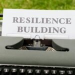 Vintage typewriter with 'Resilience Building' text on paper, set outdoors on grass.
