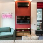 Interior of modern office lounge zone with sofa and armchair with table near window next to TV on wall and neon signboard with text do what you love near door