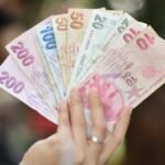 A hand displays several denominations of Turkish Lira banknotes in an outdoor setting, showcasing currency diversity.