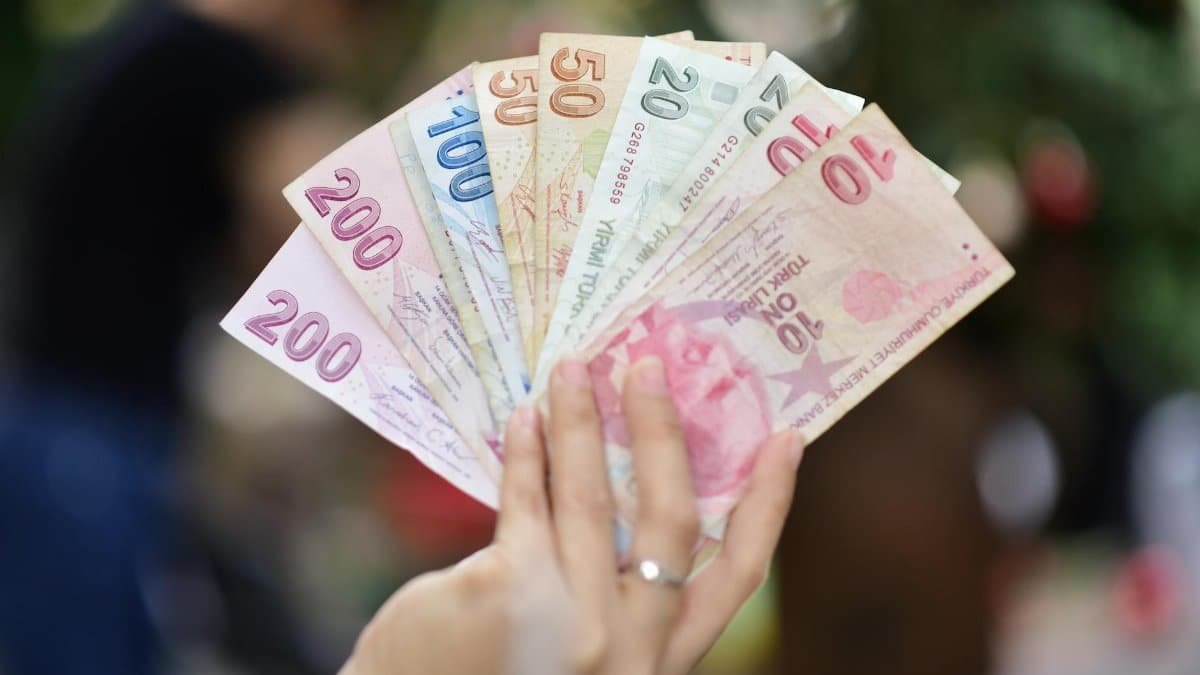 A hand displays several denominations of Turkish Lira banknotes in an outdoor setting, showcasing currency diversity.