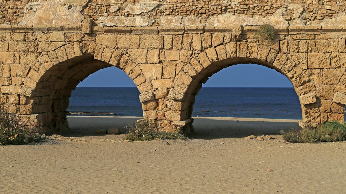 View of the ancient Roman aqueduct on the beach at Caesarea, Israel, with the sea in the background.