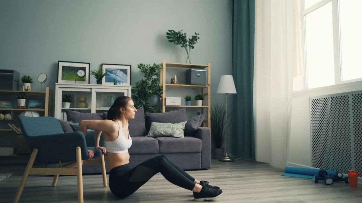 Woman doing tricep dips at home using a chair for support, promoting fitness indoors.