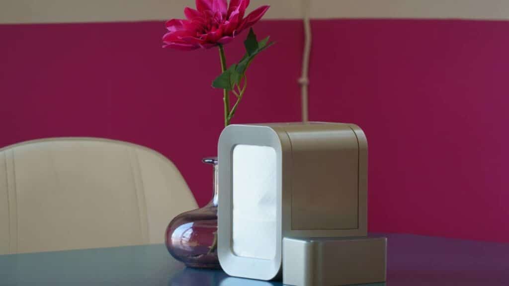Elegant interior setting featuring a sleek air purifier and vibrant pink flower in a vase on a table.