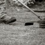 A worker uses a string trimmer to maintain a lawn, focusing on the grass edges outdoors.