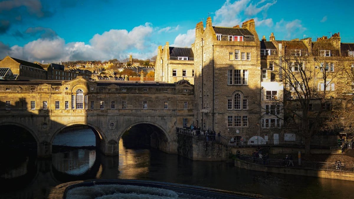 A picturesque view of the historic Pulteney Bridge in Bath, captured on a sunny day with clear blue skies.