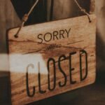 Through glass of wooden signboard with inscription Sorry We Are Closed hanging on doors of shop