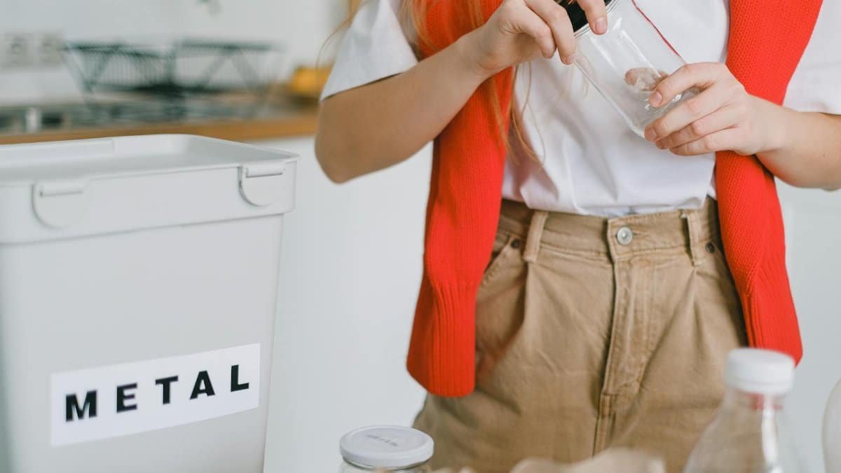 A woman sorts recyclables in an eco-friendly kitchen setup, focusing on metal and glass.