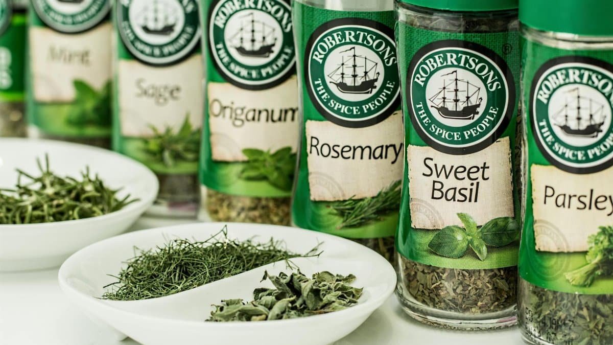 Assorted dried herbs in branded spice jars with bowls of loose herbs in the foreground.