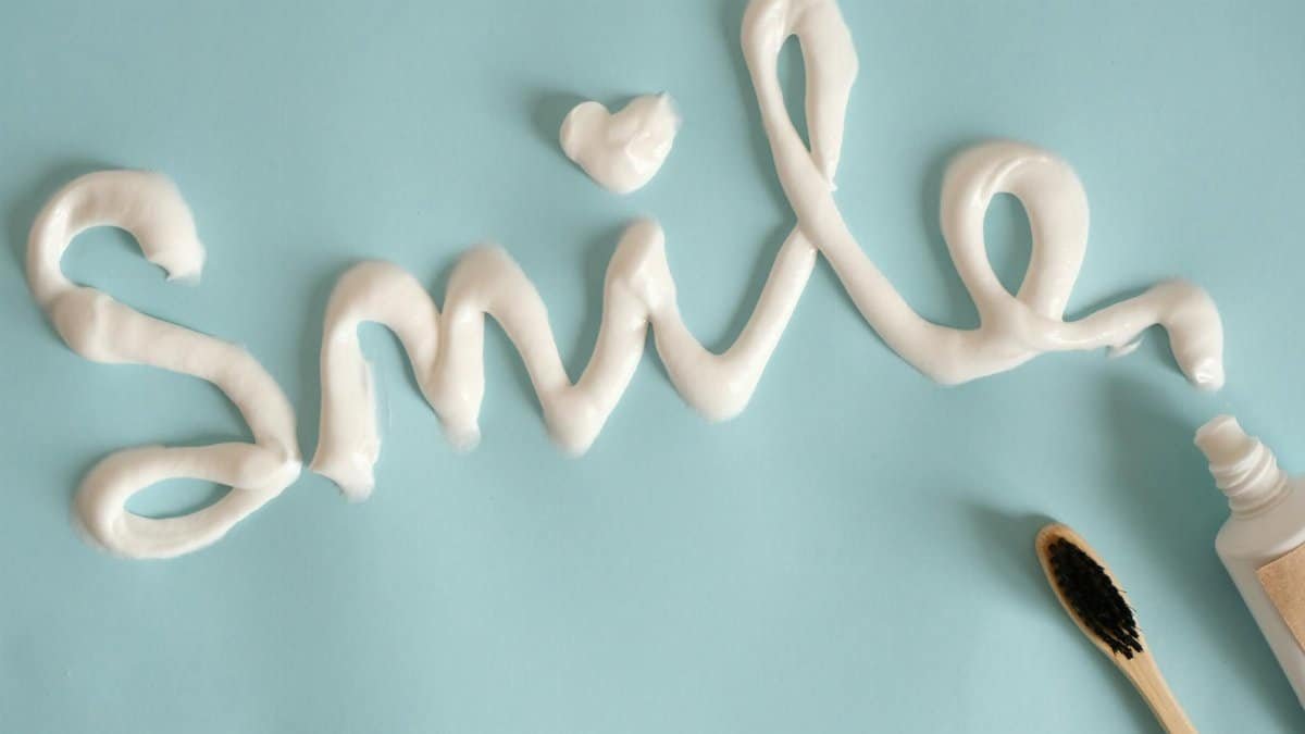Toothpaste spelling 'Smile' on turquoise surface with toothbrush.