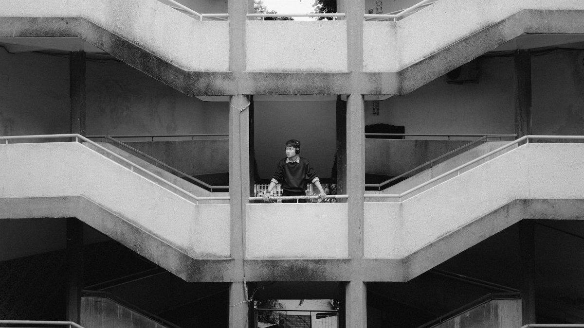 A man stands on a concrete staircase in a black and white urban setting.