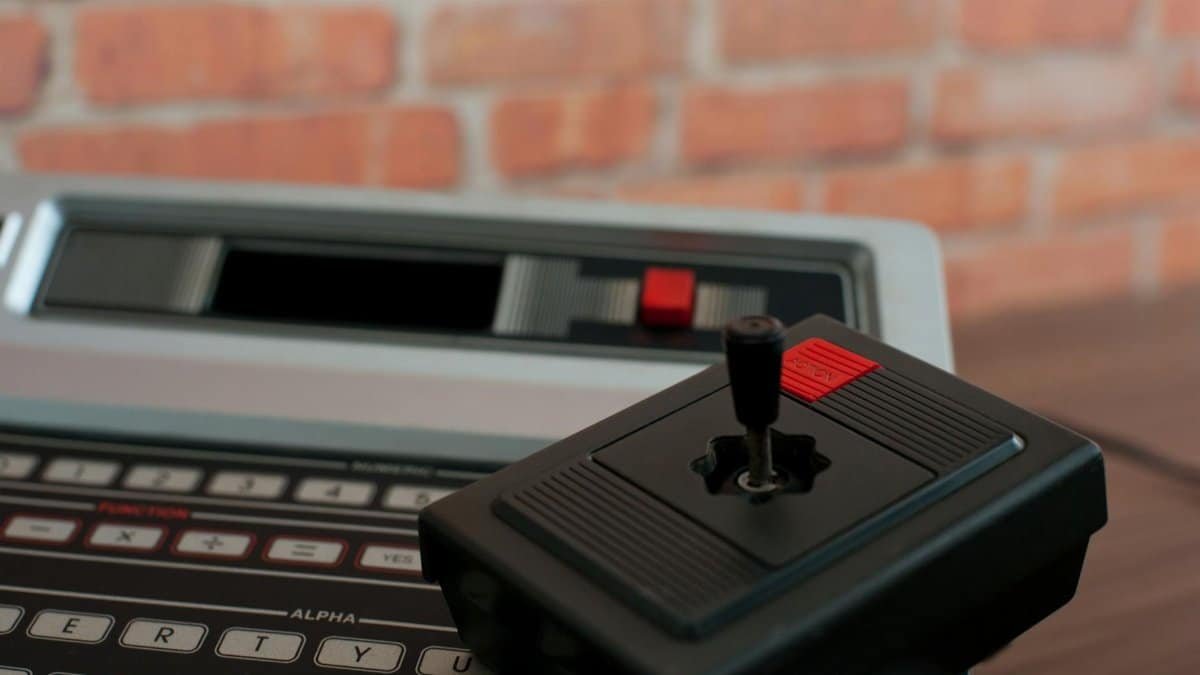 A close-up of a vintage Philips Odyssey 2 game console and joystick against a brick wall.
