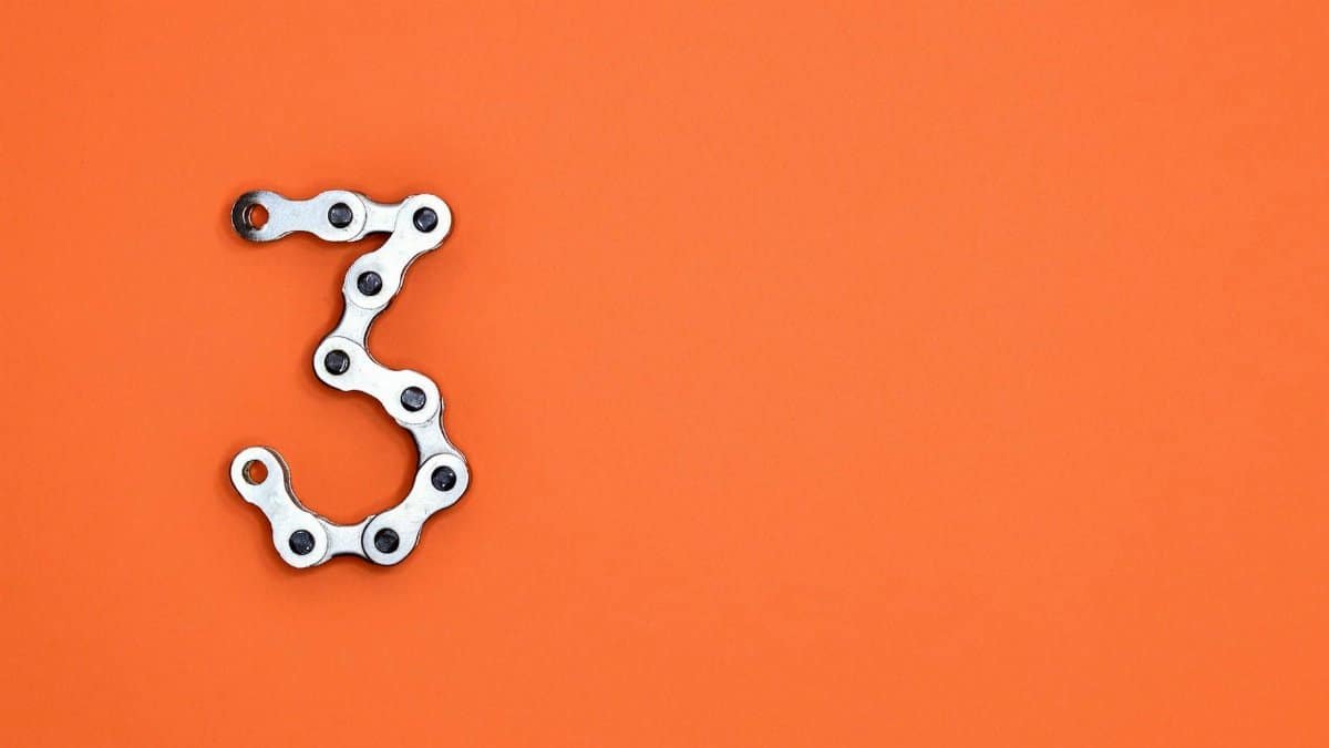 A bicycle chain forms the number three against a vibrant orange backdrop, offering ample copyspace.
