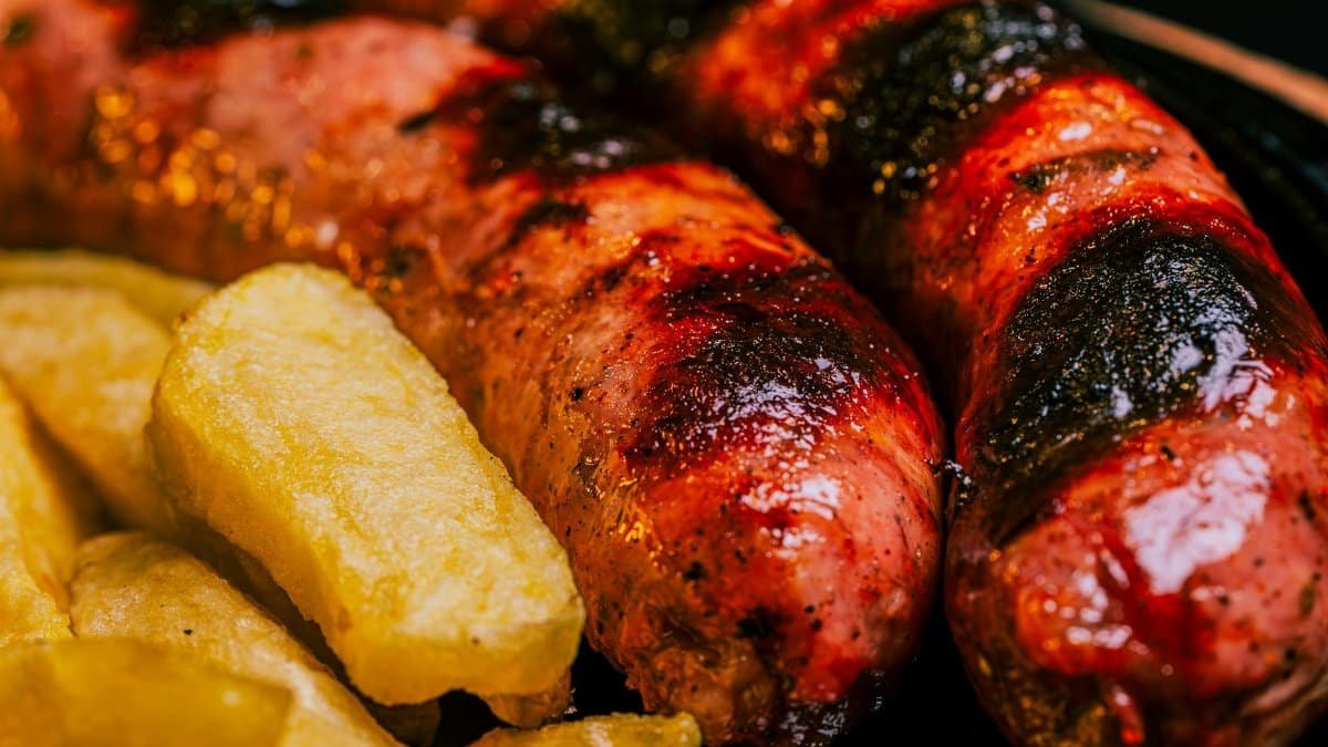 Close-up of perfectly grilled sausages and golden potato wedges. Ideal for barbecue lovers.
