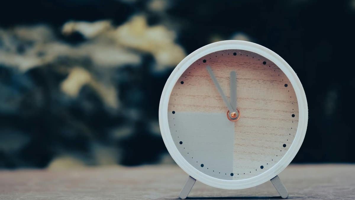 Round wooden analog clock with a minimalist design on an outdoor surface.