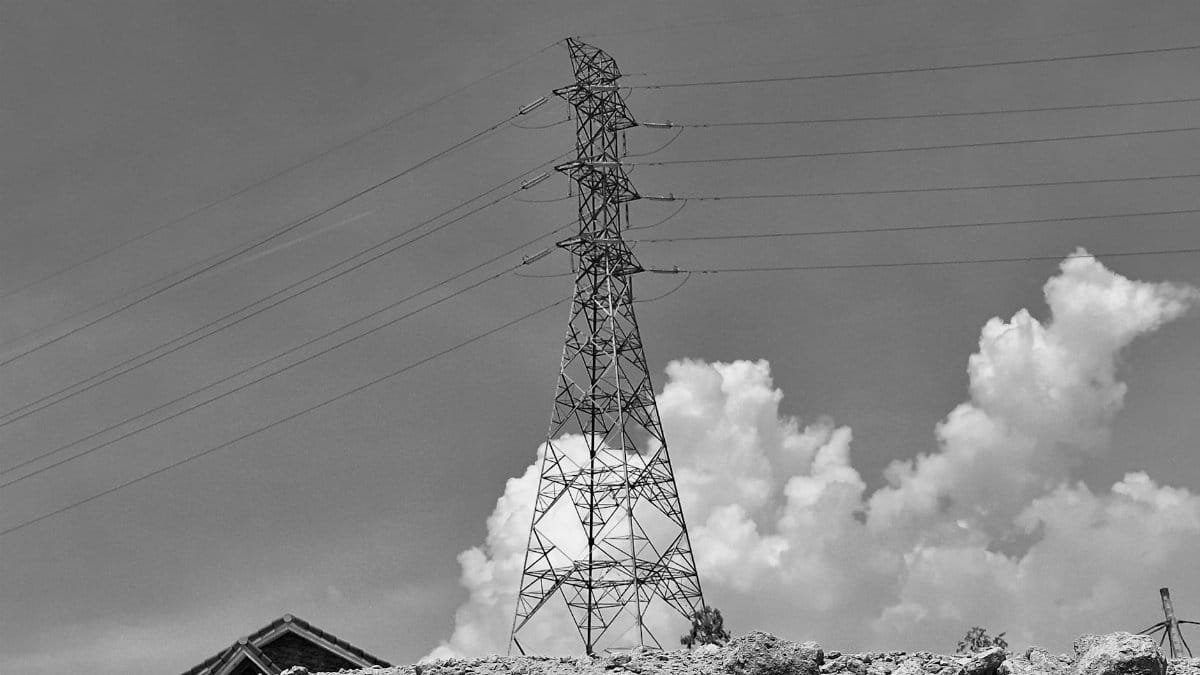 Black and white photo of a power line tower with clouds and rubble in the foreground, creating a moody atmosphere.