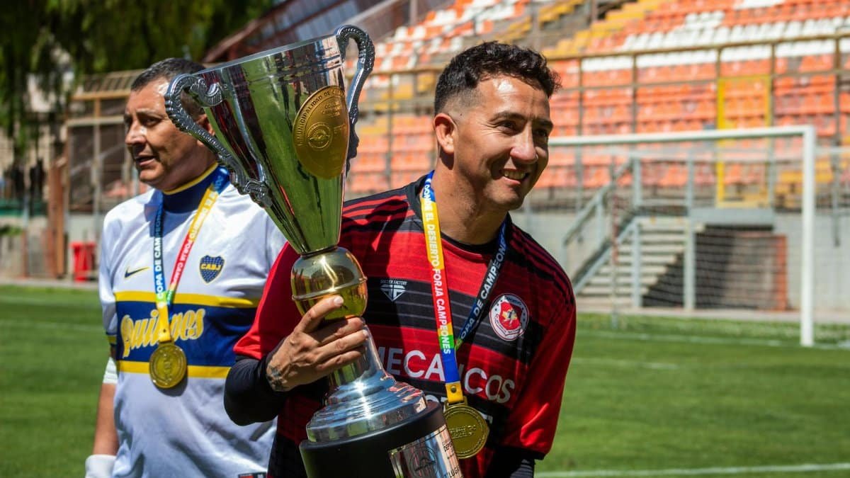 Two soccer players celebrate with a championship trophy on the field.